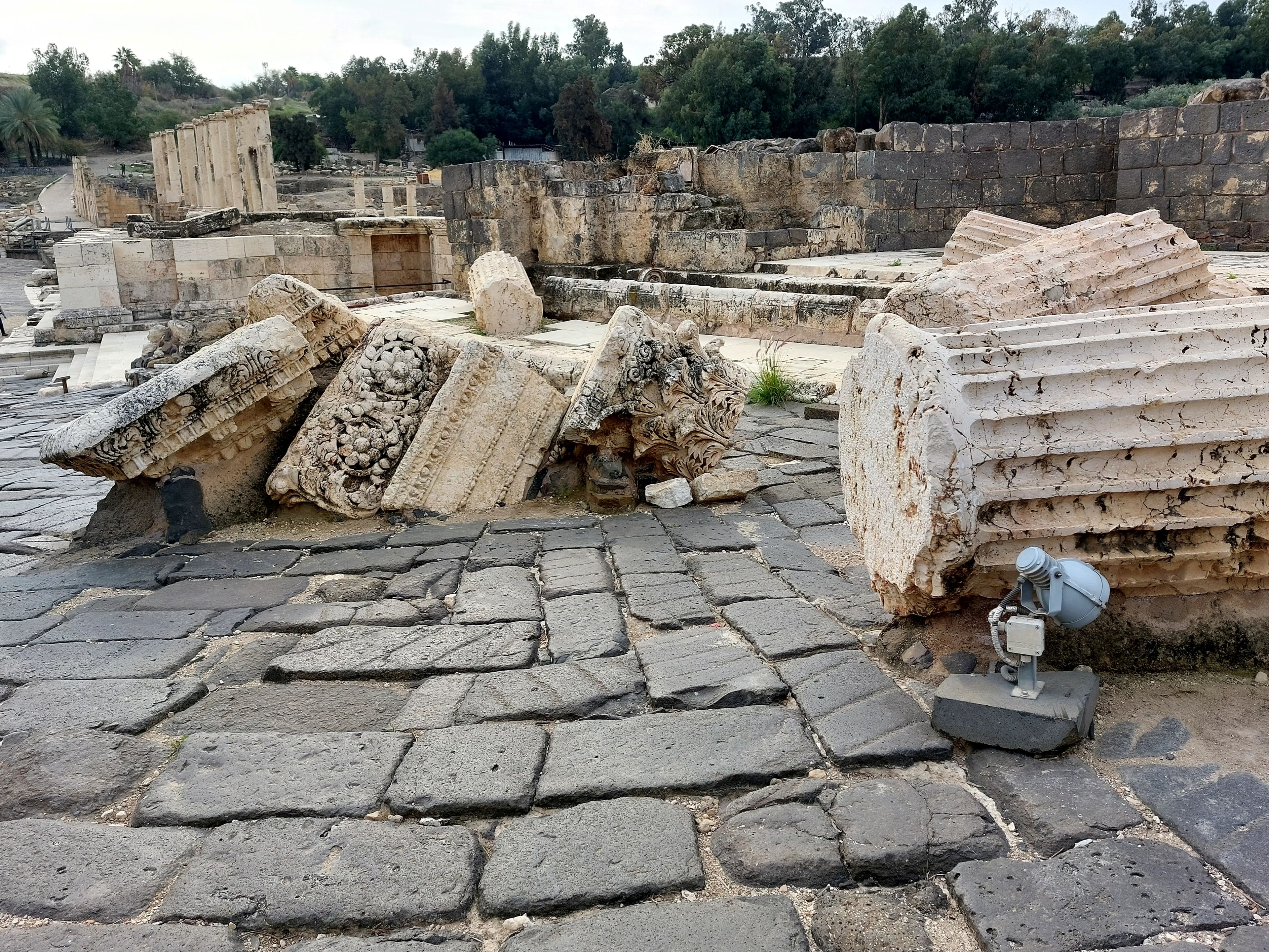 Ornate carved Roman column capitals and architectural fragments toppled and lying on the ancient basalt paving stones at Beth-Shan, left exactly where they fell when the 749 A.D. earthquake struck and the city was abandoned