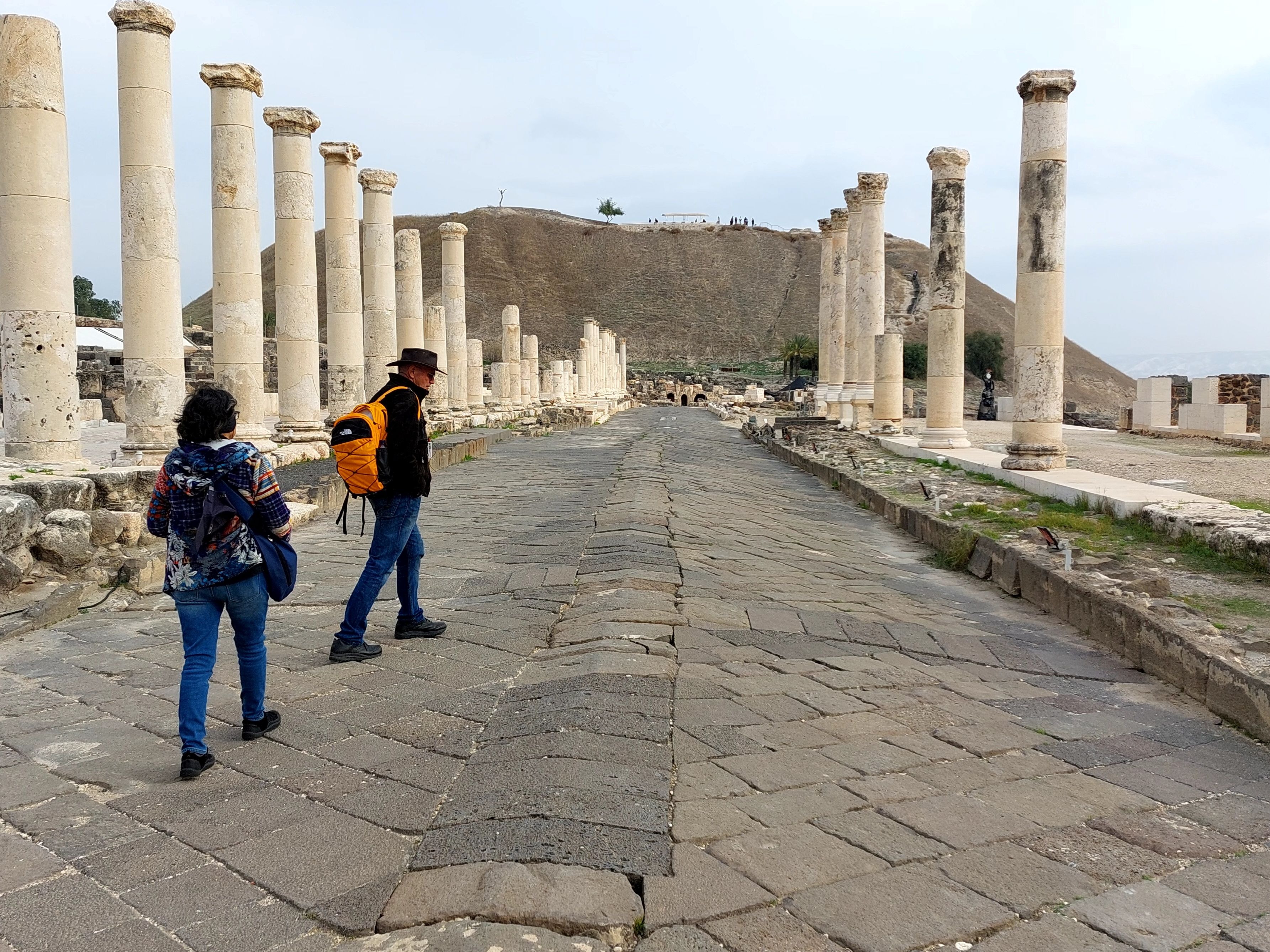 Two visitors walking along the Roman colonnade at Beth-Shan with the ancient tel mound rising in the background