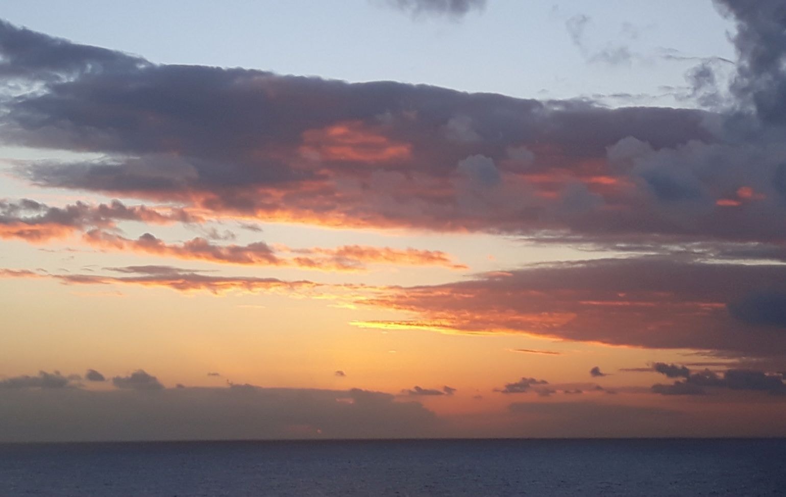 Dramatic ocean sunset with vivid orange and rose clouds over calm water