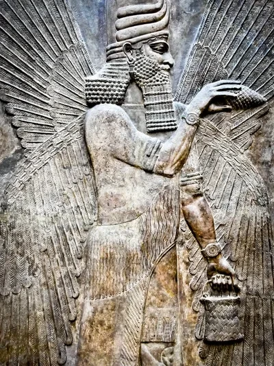 Ancient Assyrian stone relief carving of a winged divine figure with ornate headdress — a protective spirit or apkallu from the palace of an Assyrian king