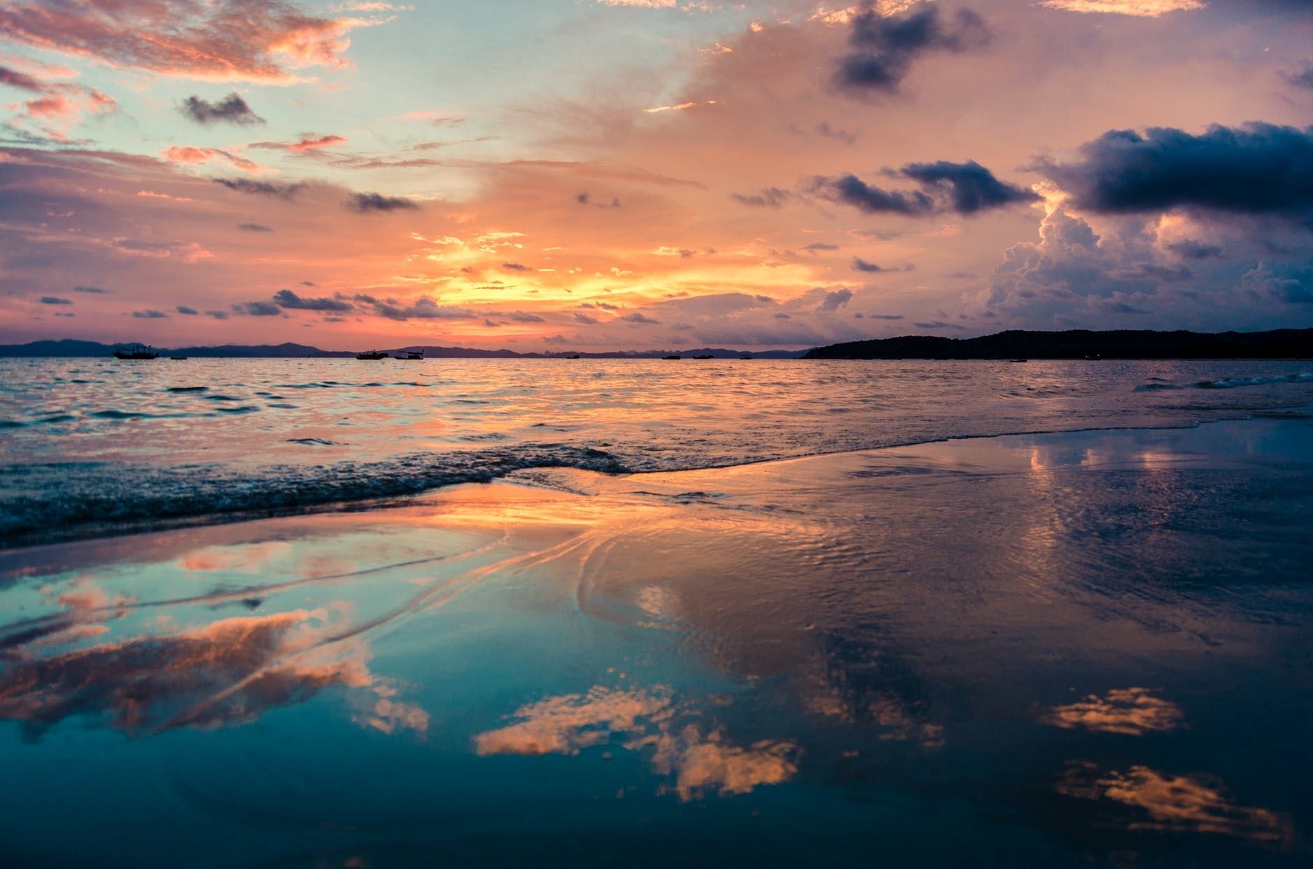 Vibrant sunset over the ocean with clouds reflected in wet sand on the beach