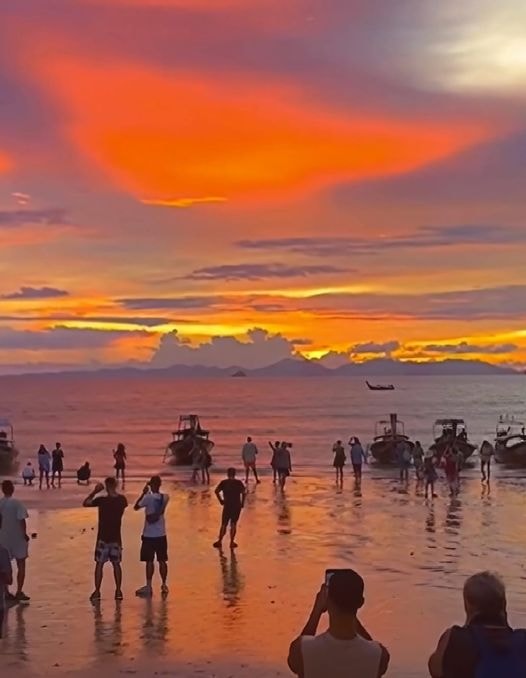 Dramatic fiery orange and red sunset over the ocean with people gathered on the beach