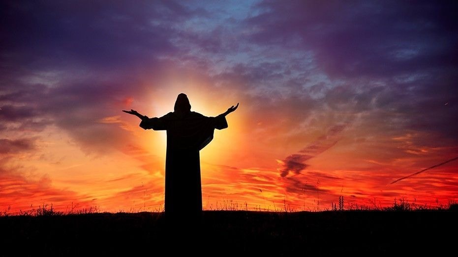 Silhouetted figure with arms raised against a dramatic fiery sunset sky