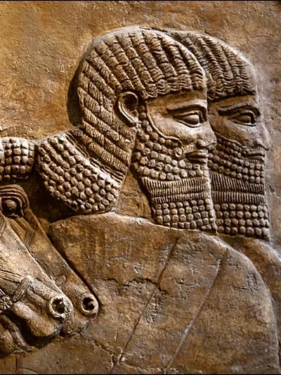 Close-up of an ancient Mesopotamian stone relief carving showing two bearded figures in profile — detailed Neo-Assyrian or Neo-Babylonian palace relief